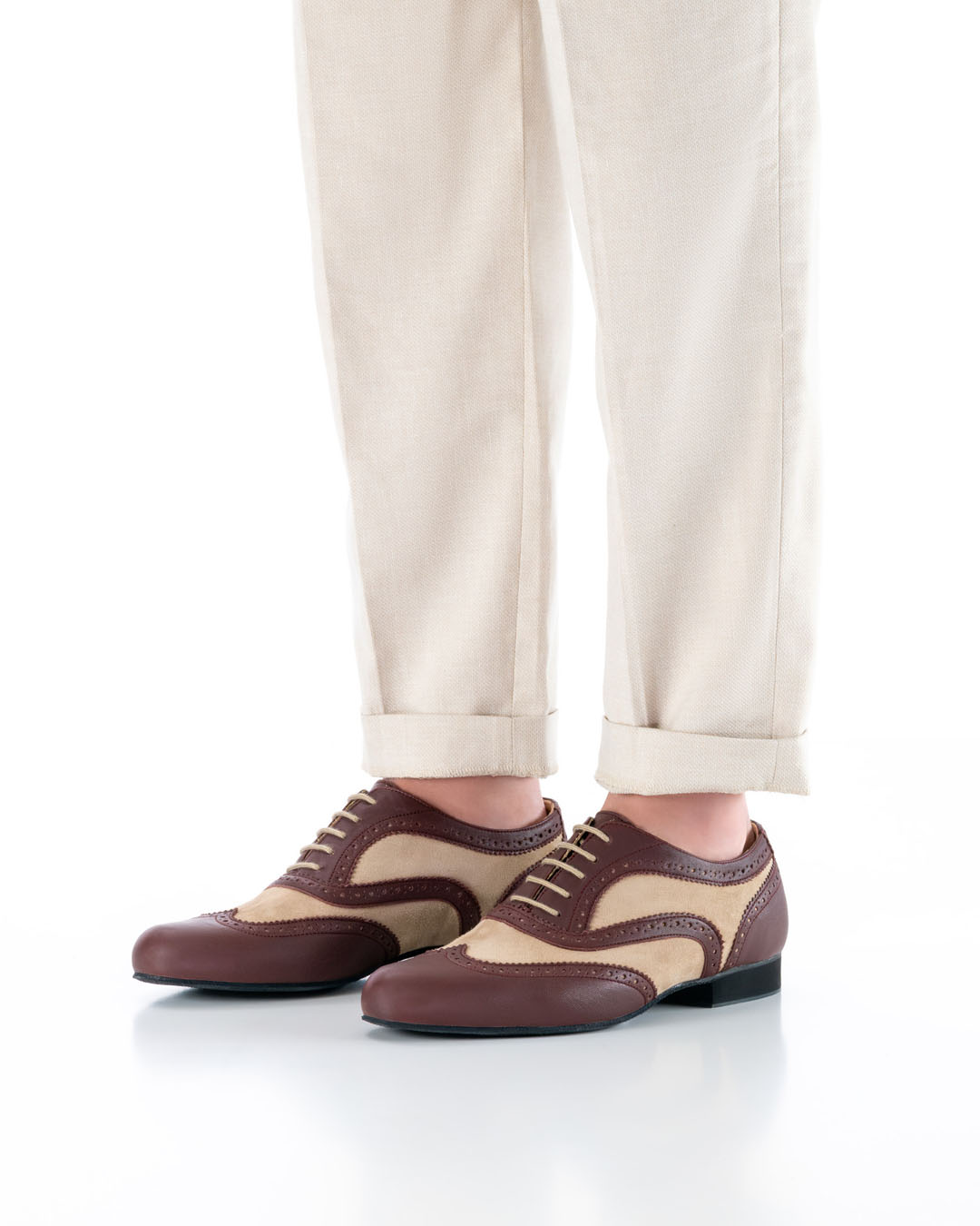 La modelo está de pie, con los pies paralelos y unos pantalones claros, en posición diagonal respecto a la cámara, y lleva unos elegantes zapatos de baile de cuero en tonos beige y burdeos, con diseño brogue y cordones claros.