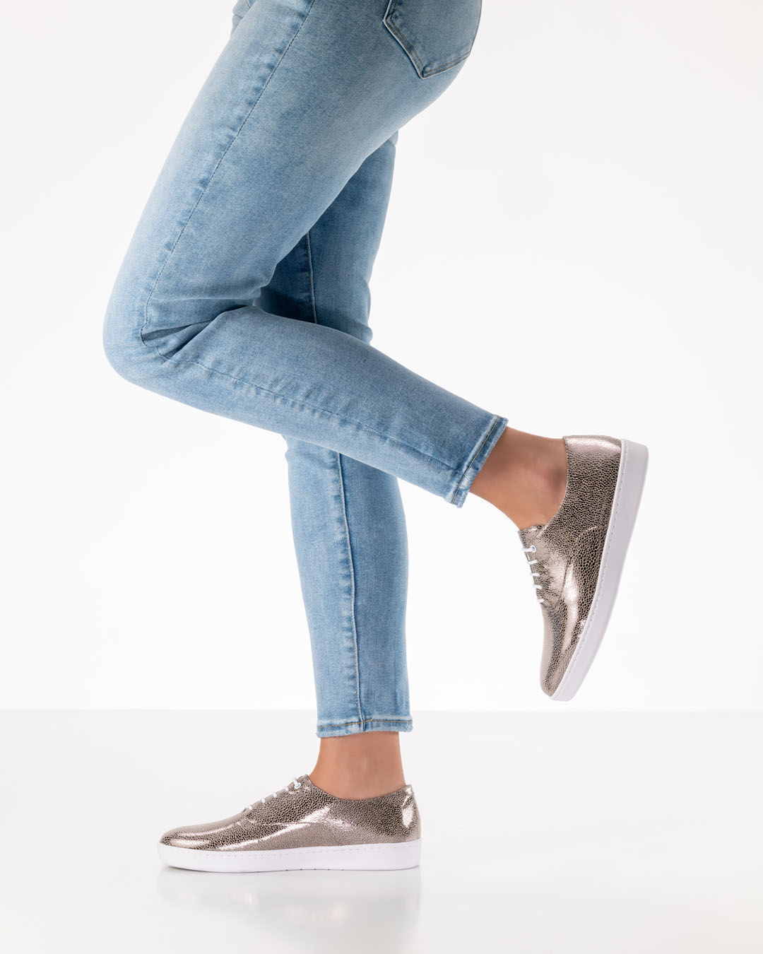 Piernas de una modelo de zapatos de baile con vaqueros claros y zapatos de baile de color platino con cordones y suela de PU blanca