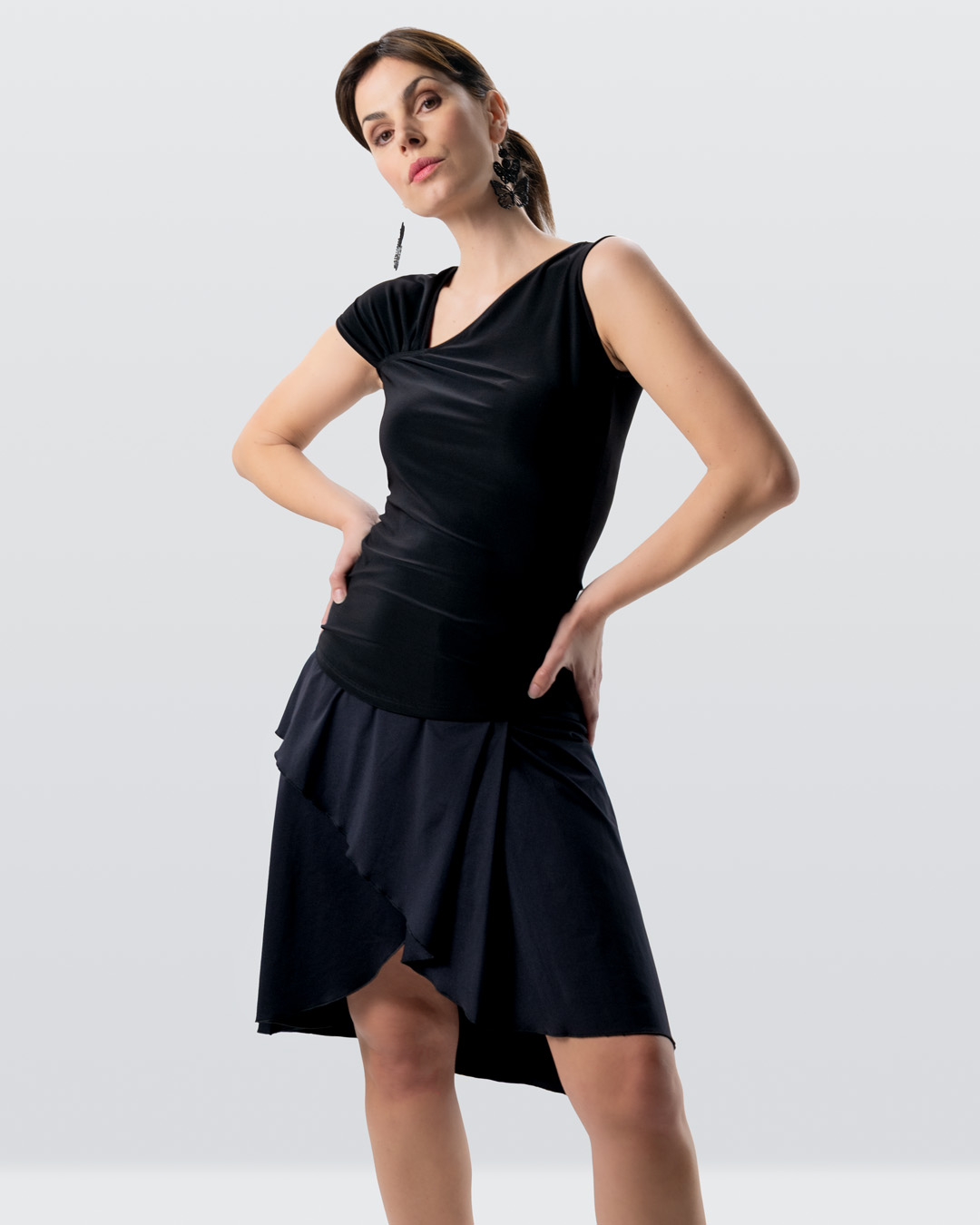 Modelo posando en el estudio con el conjunto de baile compuesto por la falda Vana y el top Yari en color negro.