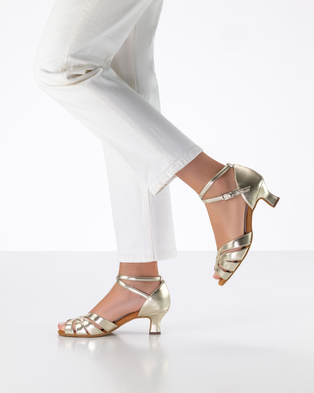 La modelo está de perfil y levanta un pie hacia atrás con unas sandalias doradas de baile de Anna Kern.