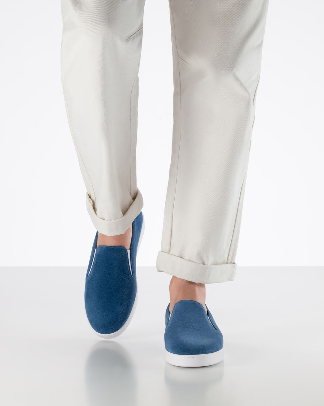 La modelo camina hacia la cámara con pantalones blancos y zapatillas de baile azules de ante con suela blanca.
