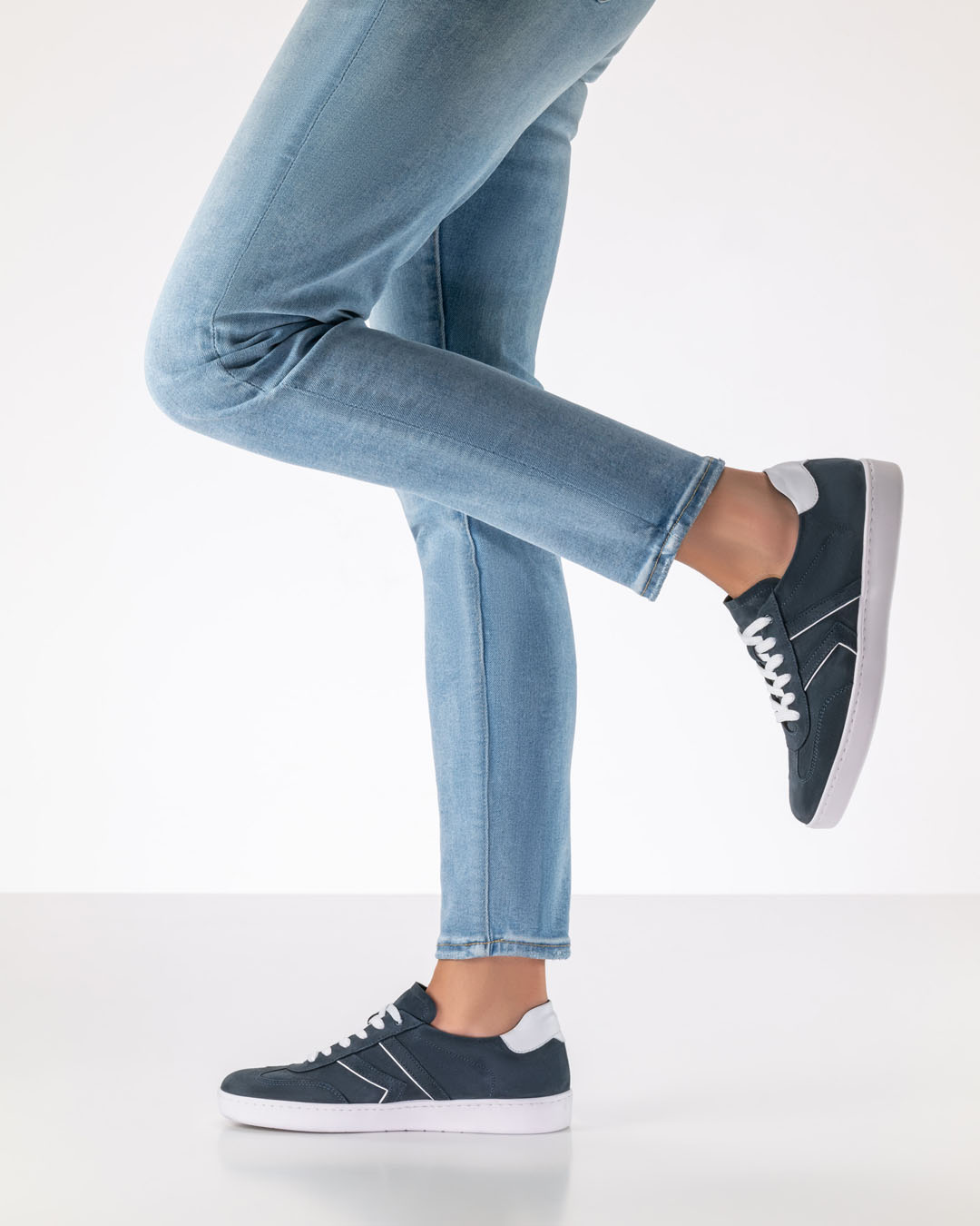 La modelo está de perfil y lleva unos vaqueros claros y ajustados y unas zapatillas de ante azul oscuro con suela blanca.