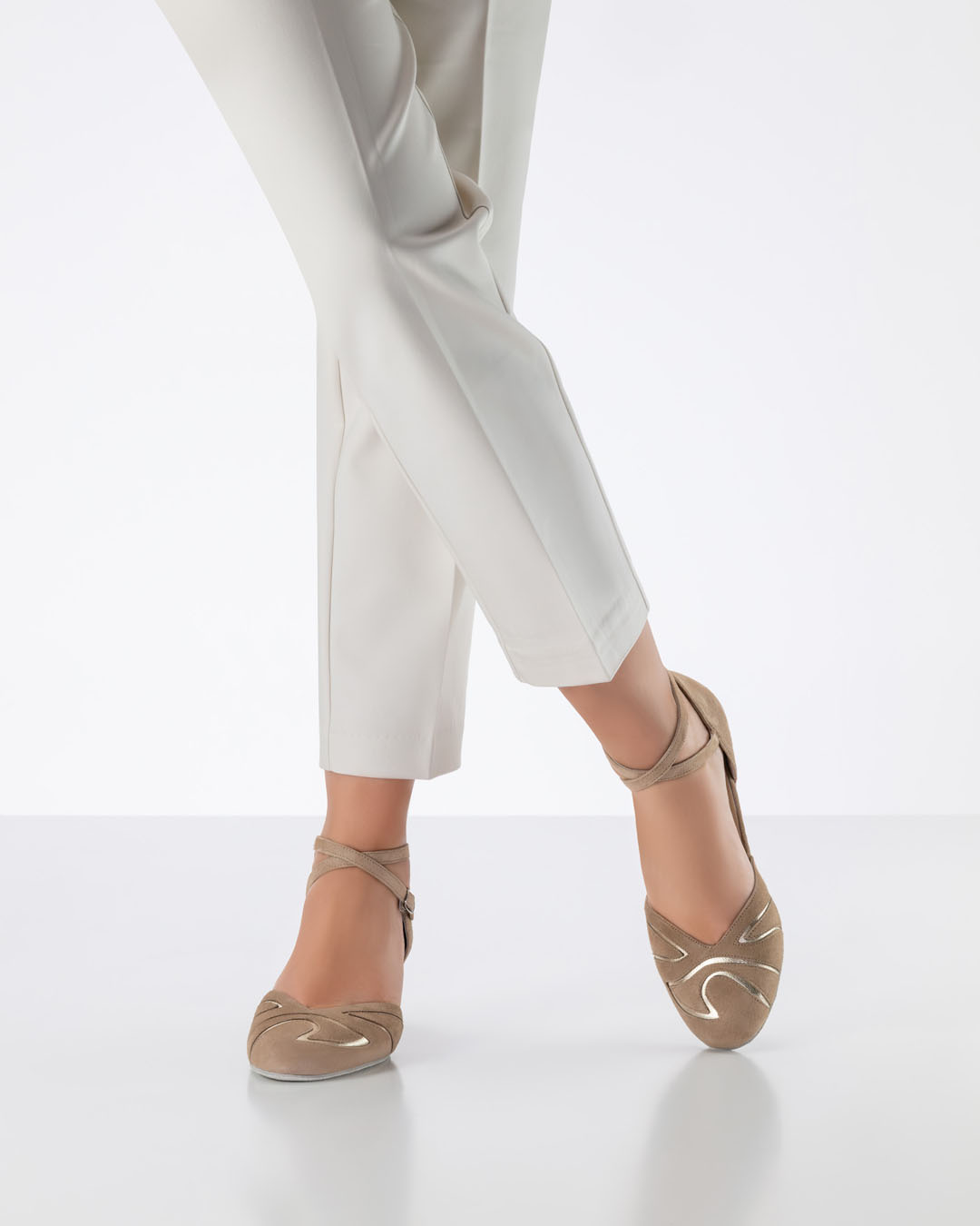 Una modelo con pantalones de color beige claro cruza las piernas y lleva unas zapatillas de baile cerradas de color beige de Werner Kern.