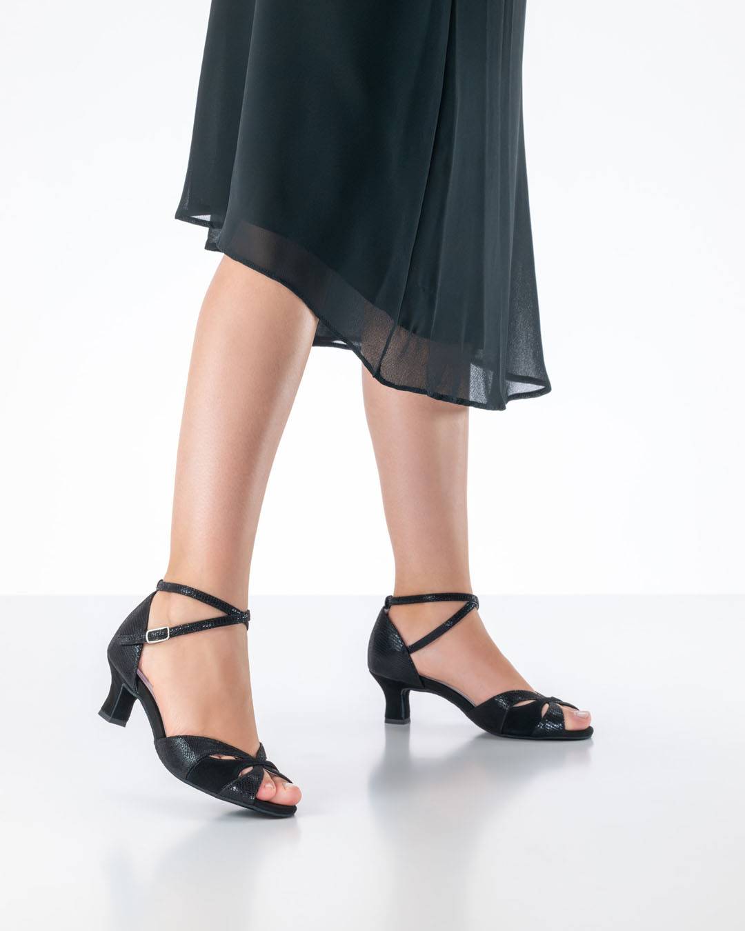 Una modelo con un vestido de gasa negro luce las sandalias de baile negras «Eunice» de Anna Kern, con tacón Flarab de 5 cm.