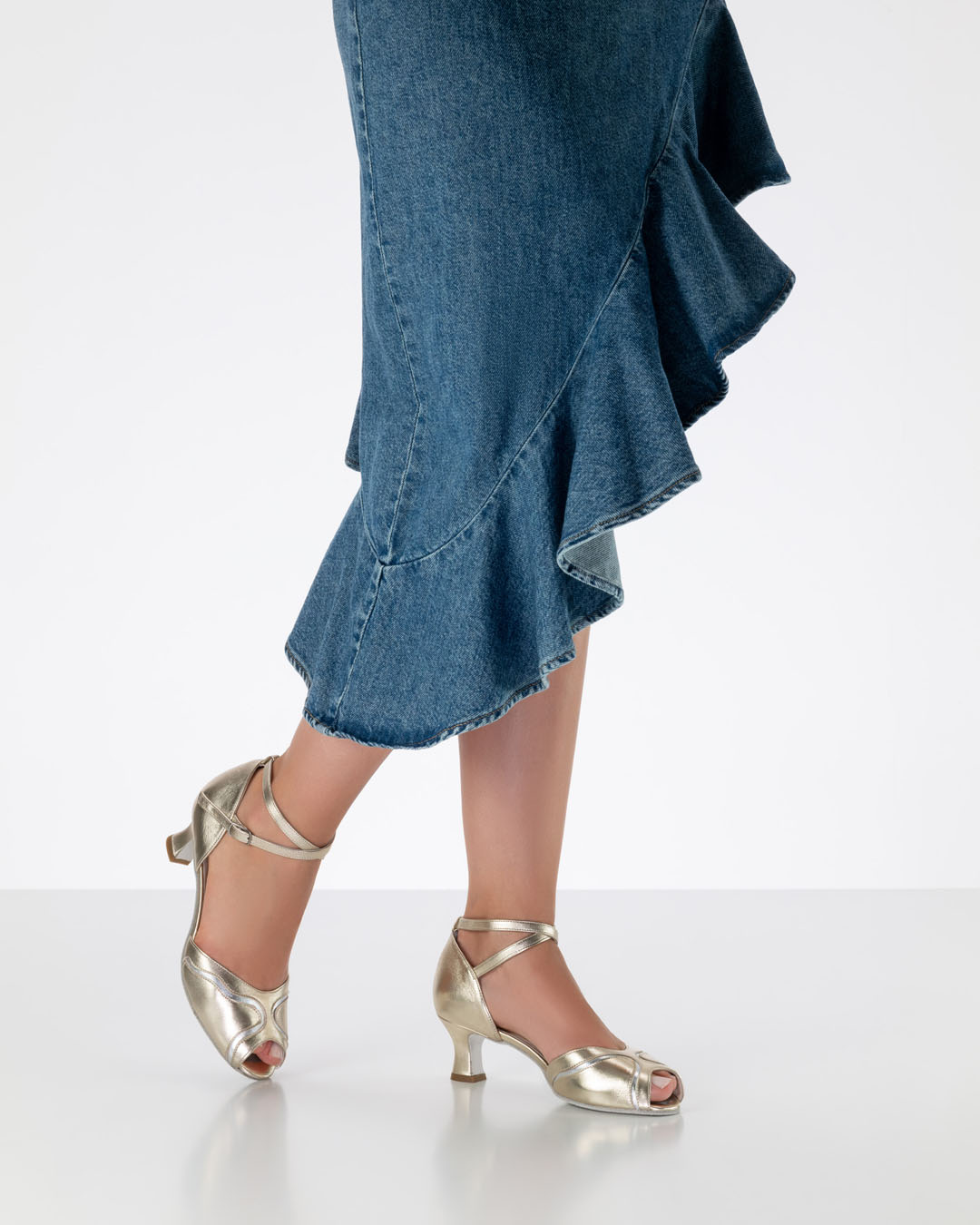 Una modelo con una falda con volantes luce unas sandalias doradas de baile con detalles plateados