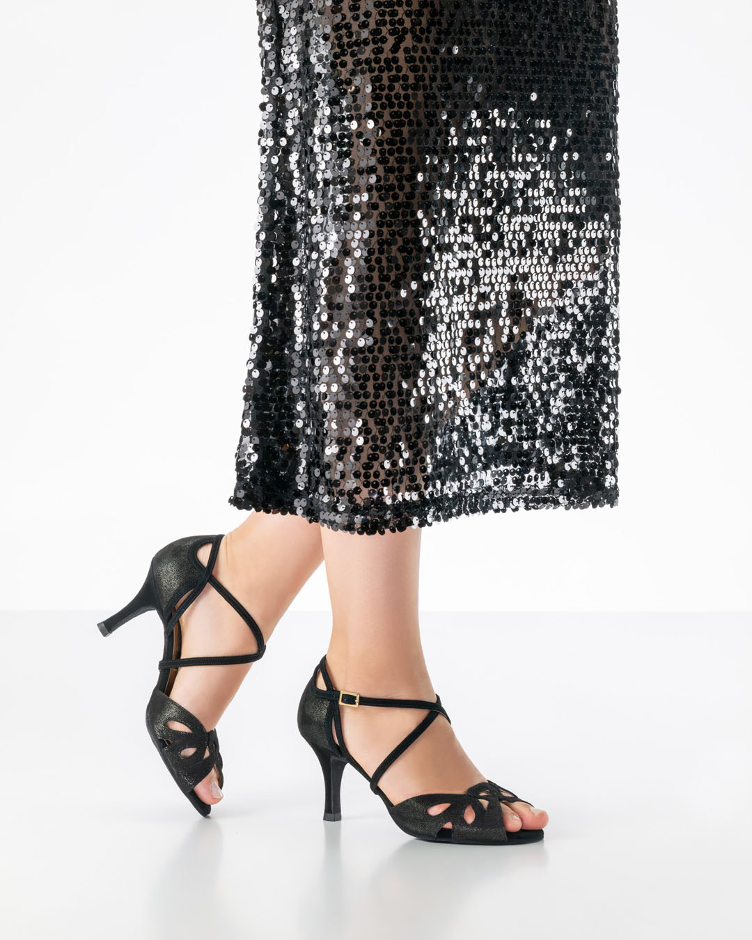 Elora: zapato de baile abierto, de color negro brillante y con tacón de 7 cm de Nueva Época, combinado con un vestido largo negro de lentejuelas.